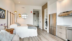Ein modernes Schlafzimmer mit Bett, Nachttisch und Spiegel. Es gibt eine Küchenzeile mit Kühlschrank und Herd.