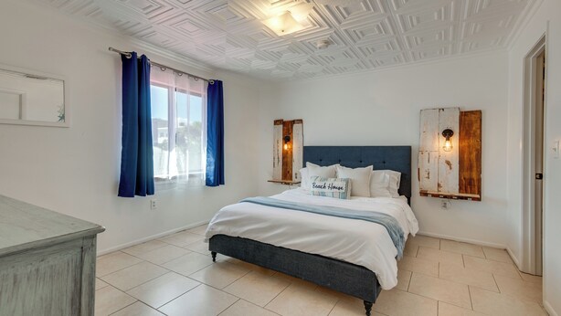A bedroom with a bed, a window with curtains, a wall-mounted light fixture, and a door. - Beach Retreat w/ Pool Near Rocket Launches (Cape Canaveral)