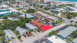 An aerial view of a coastal residential area with a prominent red-roofed building, surrounded by other houses and a beach in the background. - Beach Retreat w/ Pool Near Rocket Launches (Cape Canaveral)
