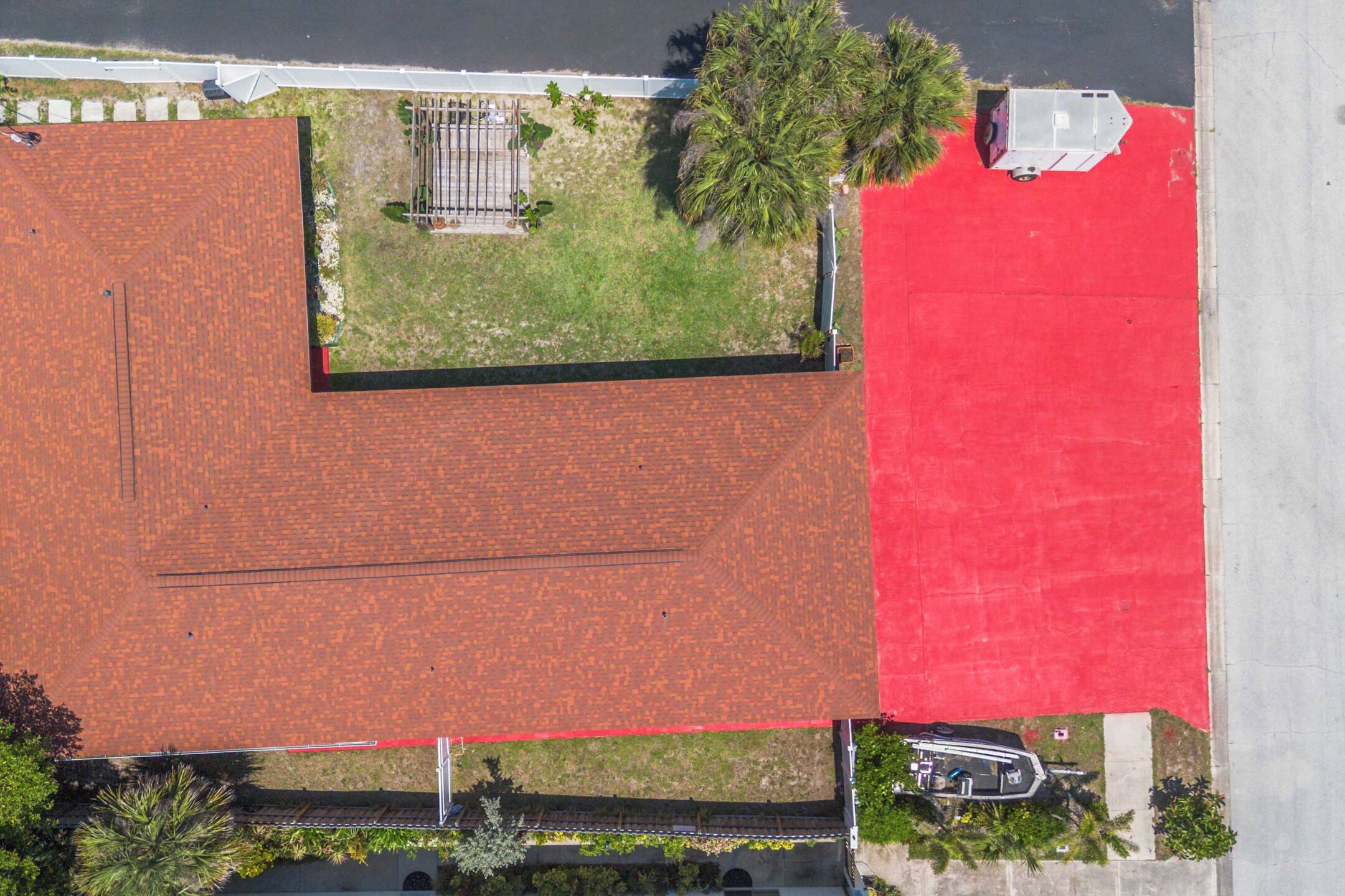 An aerial view of a building with a red roof, a parking area, and a small garden with a fence.