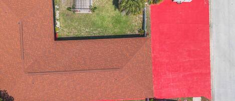 An aerial view of a building with a red roof, a parking area, and a small garden with a fence.