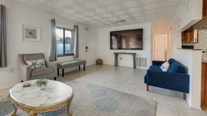 A spacious living area with a large flat-screen TV, a grey sofa, a blue sofa, a marble coffee table, and a bench. - Beach Retreat w/ Pool Near Rocket Launches (Cape Canaveral)