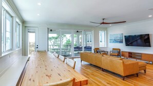 A spacious living area with a long wooden dining table, a beige sofa, and a television mounted on the wall. - Steps to Shore: Luxe Group Retreat in Port St Joe (Port St. Joe)