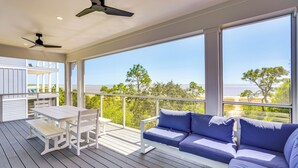 A balcony with a white table and chairs, a blue sofa, and a view of the sea. - Steps to Shore: Luxe Group Retreat in Port St Joe (Port St. Joe)