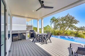 An outdoor deck with a grill, table, and chairs, overlooking a swimming pool and trees. - Steps to Shore: Luxe Group Retreat in Port St Joe (Port St. Joe)