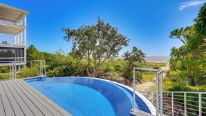 A swimming pool with a wooden deck, surrounded by greenery and overlooking a scenic view. - Steps to Shore: Luxe Group Retreat in Port St Joe (Port St. Joe)