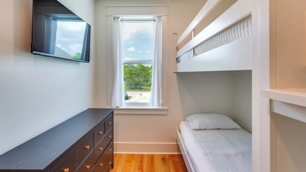 A compact bedroom with a bunk bed, a dresser with drawers, a window with curtains, and a flat-screen TV mounted on the wall. - Steps to Shore: Luxe Group Retreat in Port St Joe (Port St. Joe)