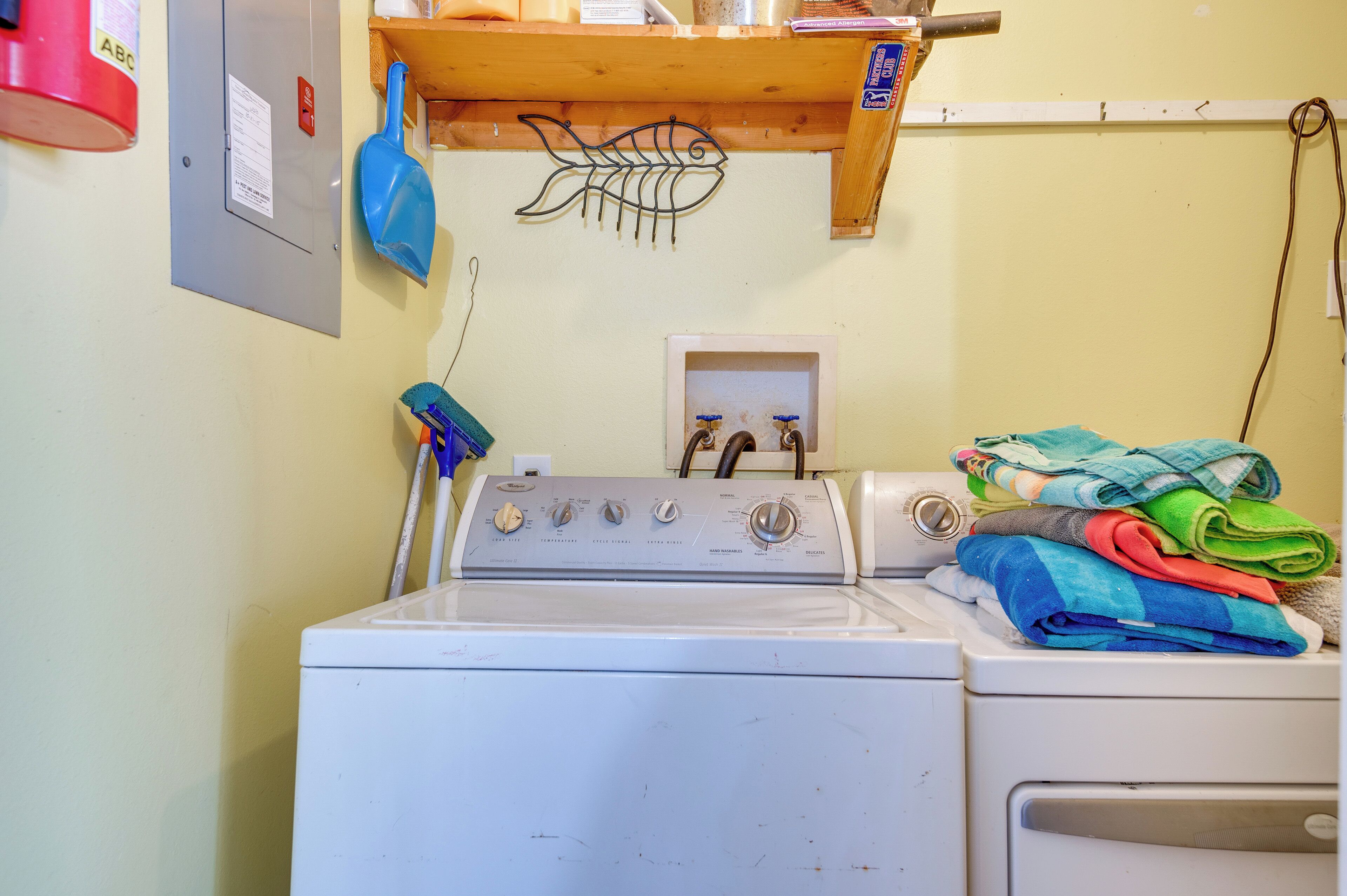 A laundry area with a washing machine, a dryer, and a wooden shelf above the washing machine.