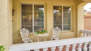 A porch with two white chairs, a small round table with a flower arrangement, and a white balustrade. - Grand & Convenient Home 7 Mi to Las Vegas Strip! (Las Vegas)