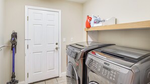 A laundry area with a washing machine and dryer, a door, and a shelf with cleaning supplies. - Grand & Convenient Home 7 Mi to Las Vegas Strip! (Las Vegas)