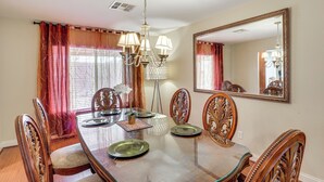 A dining room with a glass-top table, ornate chairs, a chandelier, and a large mirror on the wall. - Grand & Convenient Home 7 Mi to Las Vegas Strip! (Las Vegas)