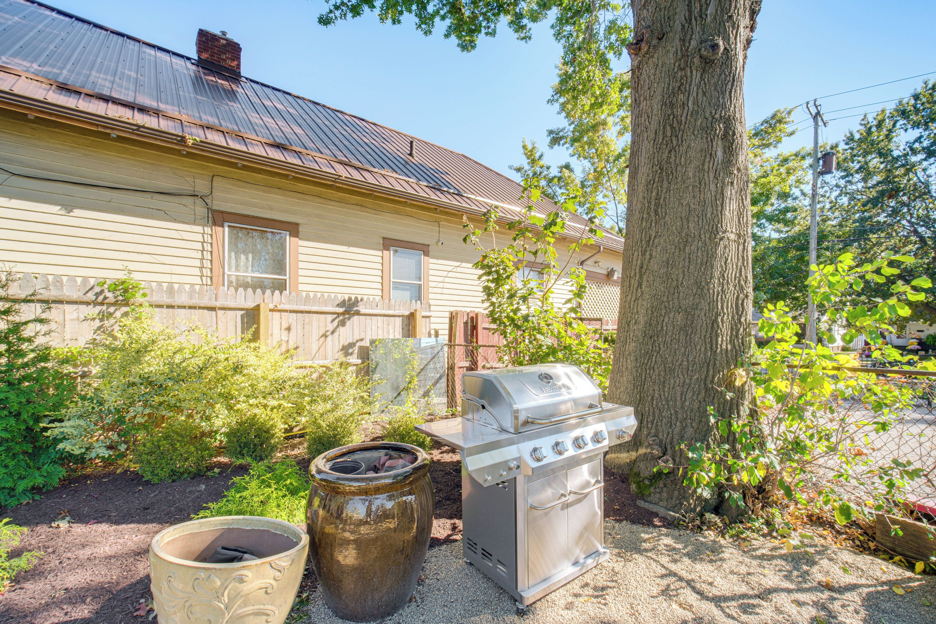 A backyard with a grill, a large pot, and a house with a metal roof.