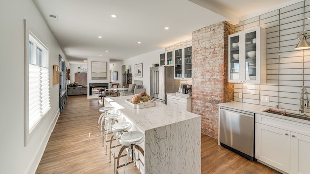 A modern kitchen with a marble island, bar stools, a brick accent wall, and stainless steel appliances. - 7 Mi to Dtwn & Lake Erie: Sleek Cleveland Apt! (Cleveland)