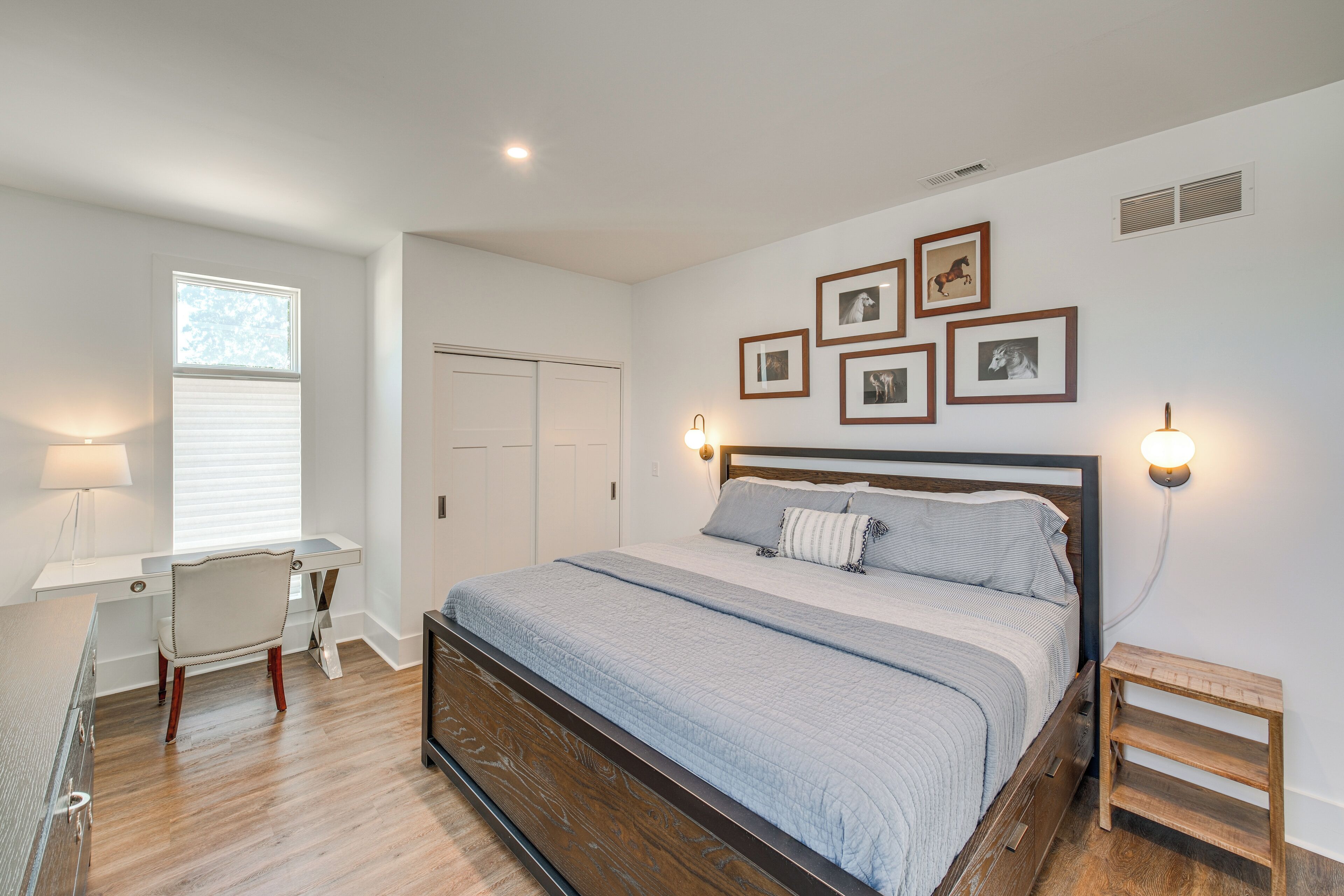 A bedroom with a bed, desk, chair, and wall-mounted lights.