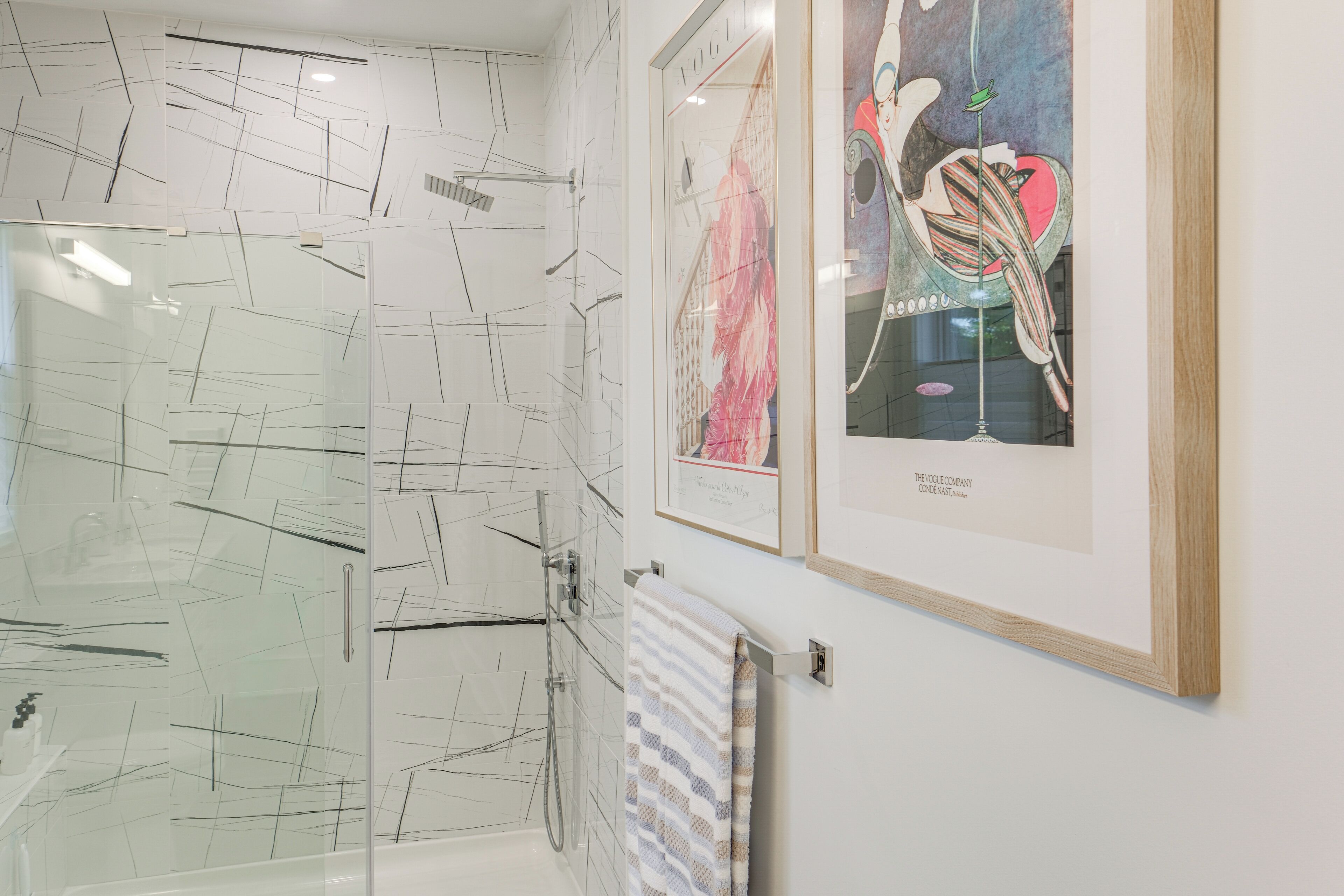 A modern bathroom with a glass shower enclosure, a framed artwork on the wall, and a towel rack.