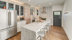 A modern kitchen with a marble island, stainless steel appliances, and a brick accent wall. - 7 Mi to Dtwn & Lake Erie: Sleek Cleveland Apt! (Cleveland)