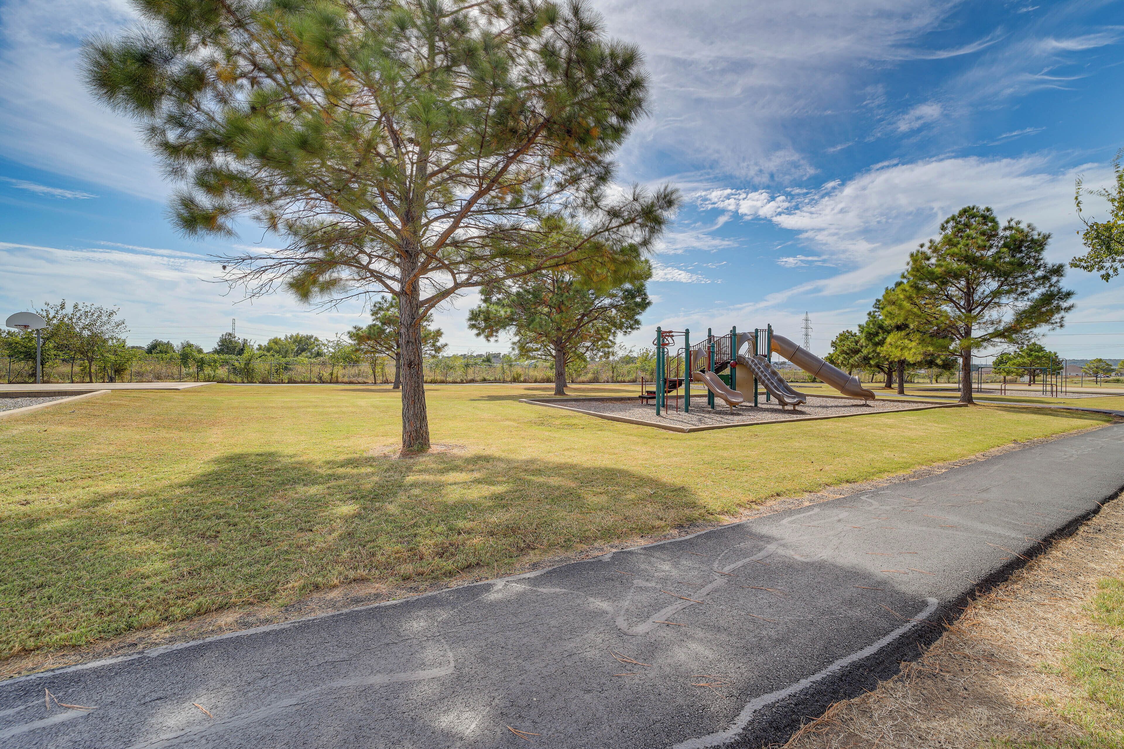 A park with a playground, a paved path, and surrounding trees.