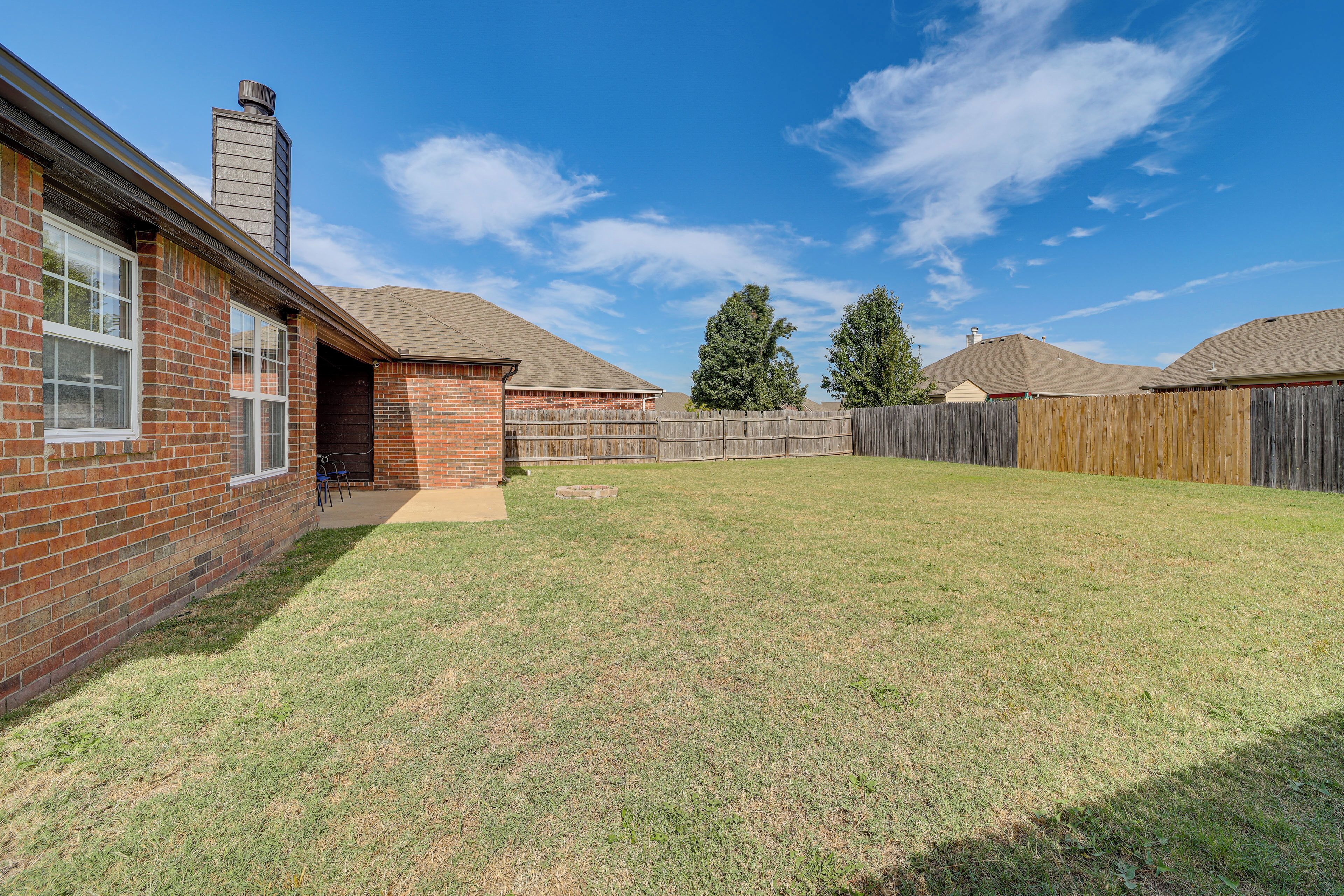 A backyard with a brick house, a wooden fence, and a clear blue sky.