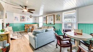 A room with a light blue sofa, wooden dining table, and chairs. There is a ceiling fan, a window with blinds, and a wall with artwork. - 2 Mi to Beach! Canal-front Escape in Crystal River (Crystal River)