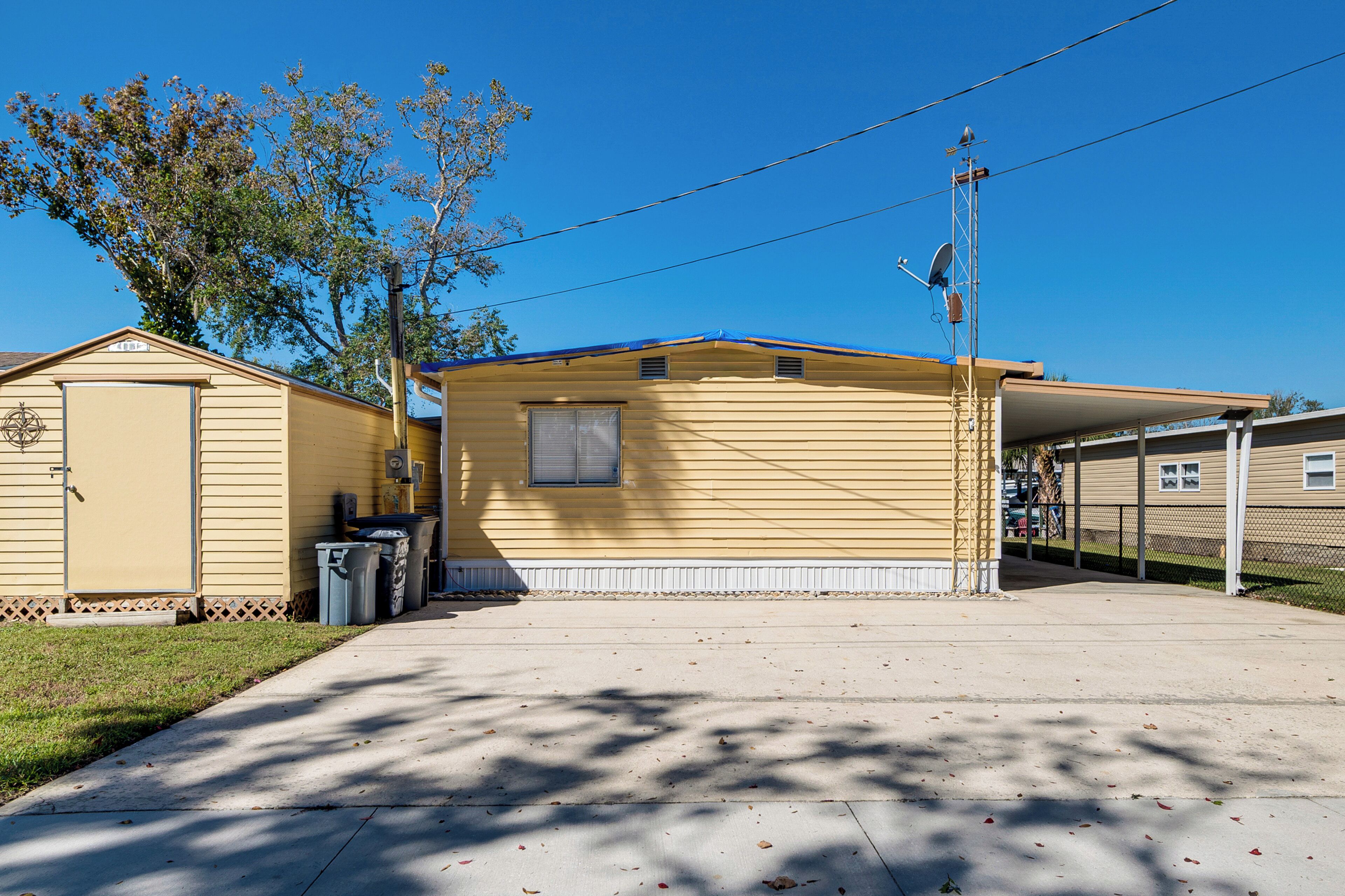A yellow mobile home with a covered patio, a garage, and a fenced yard.