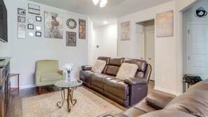 A living room with a brown leather sofa, a green armchair, and a glass coffee table. There are wall decorations including framed pictures and a globe. - Pets Welcome! Family Townhome w/ Yard in Atlanta (Atlanta)