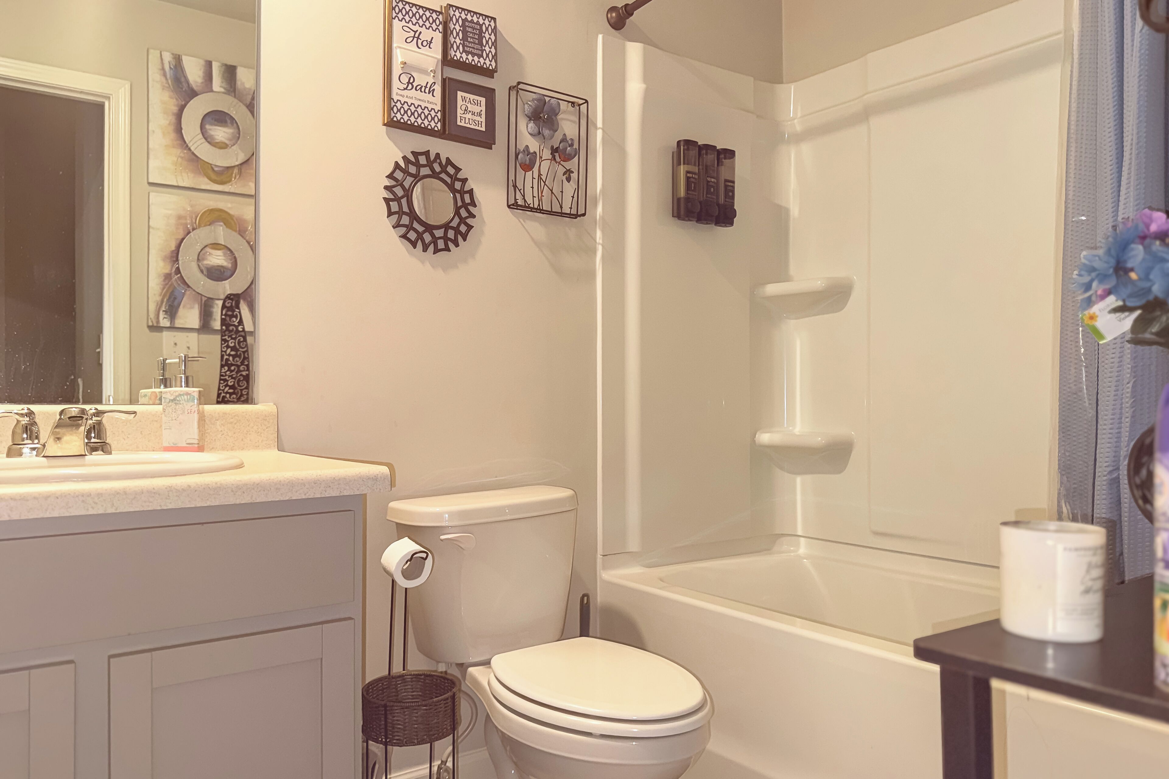 Ein Badezimmer mit Toilette, Waschbecken und Badewanne. Auf der Ablage befinden sich dekorative Wandbilder und Toilettenartikel.