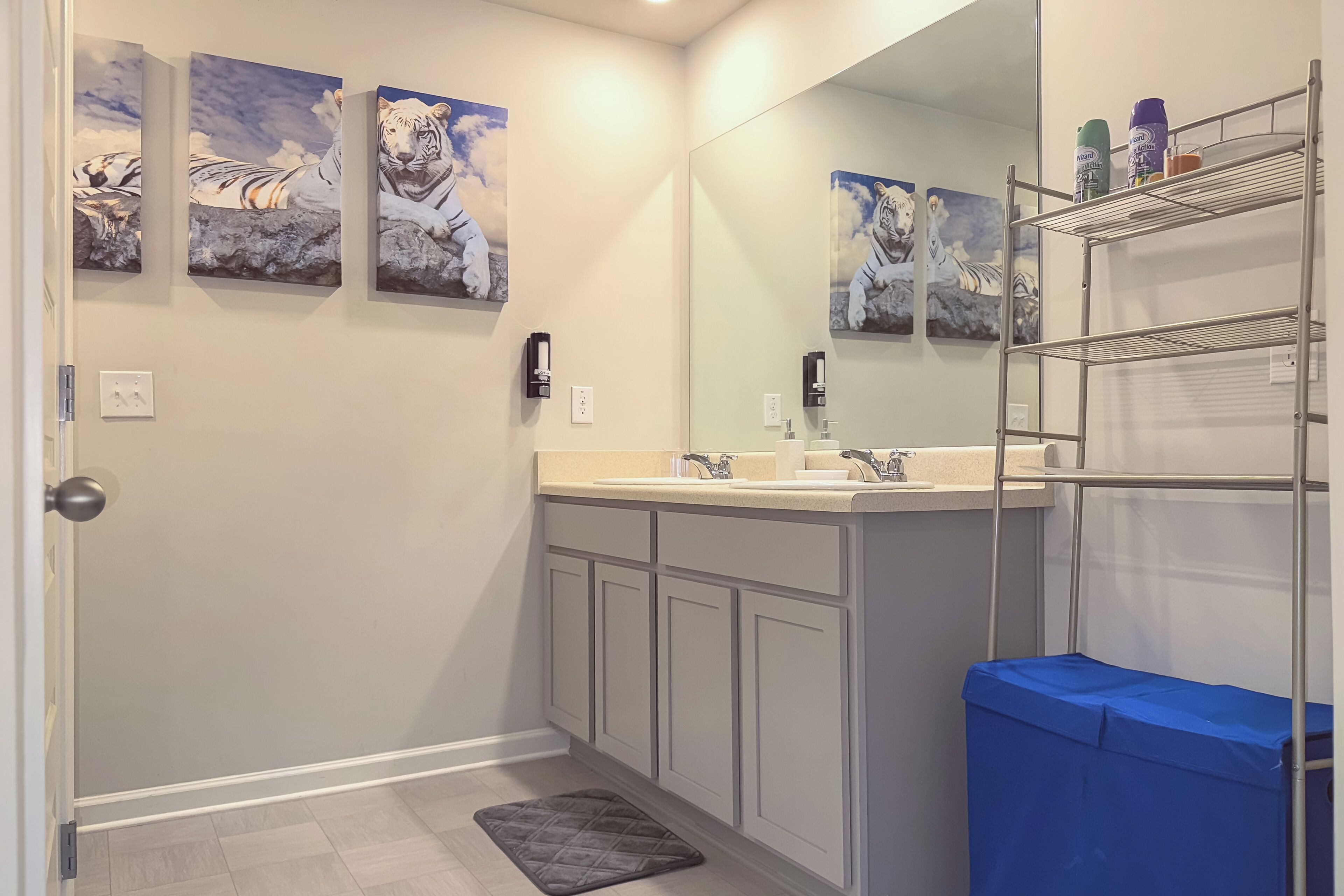 A bathroom with a white vanity, a large mirror, and three tiger paintings on the wall.