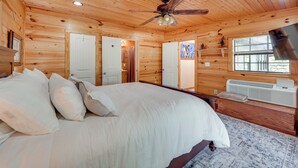 A wooden cabin bedroom with a bed, ceiling fan, and a window with blinds.