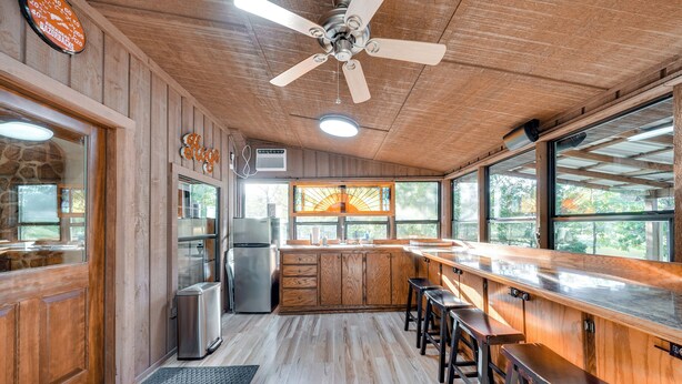 A kitchen with wooden cabinets, a bar area with stools, a ceiling fan, and large windows.