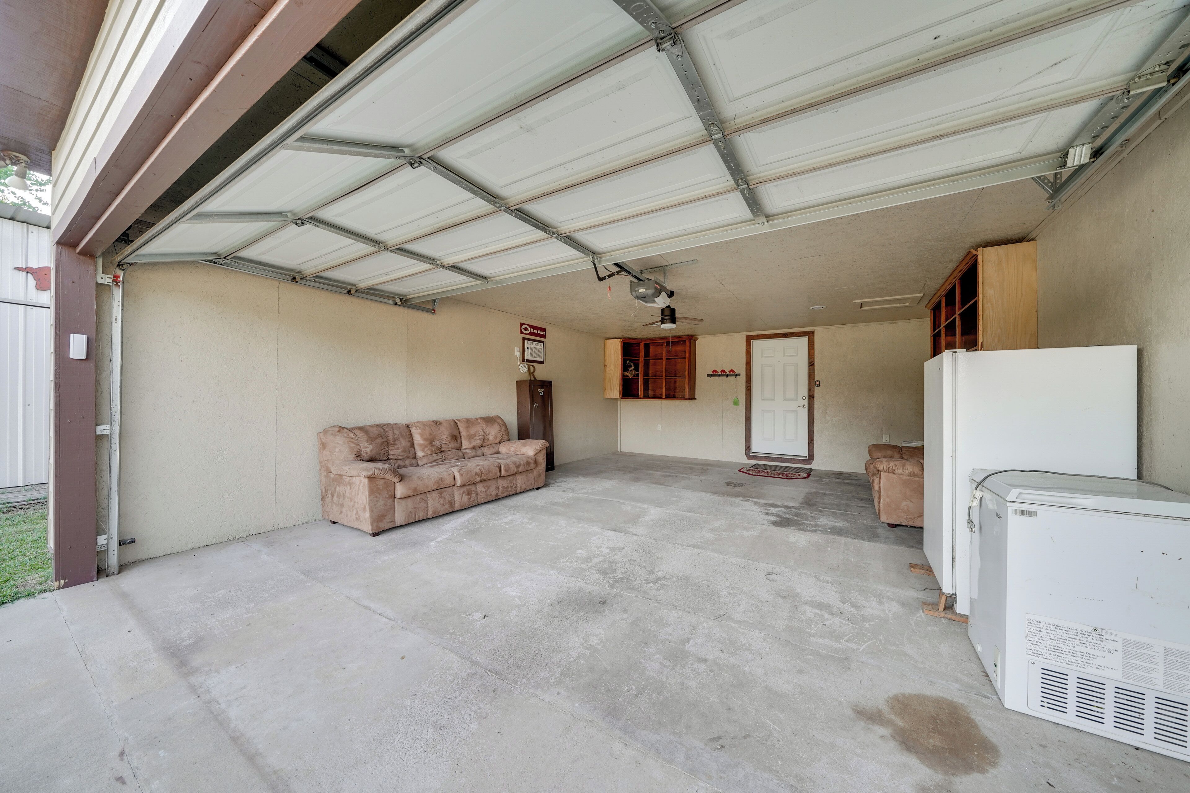 A garage with a concrete floor, a beige wall, a white refrigerator, and a brown couch.