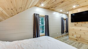 A bedroom with a wooden ceiling, a bed, two windows with curtains, and a mounted TV. - Direct Trail Access: Lyons Falls Getaway w/ Views! (Lyons Falls)