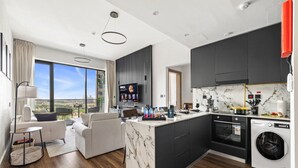 A modern kitchen with a marble island, dark cabinets, and a large window offering a city view. - New 1BR with Rooftop Pool & Amazing View (Dubai)