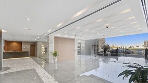 A modern hotel lobby with a reception desk, marble flooring, glass walls, and a view of the cityscape. - New 1BR with Rooftop Pool & Amazing View (Dubai)