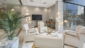 A modern living room with white furniture, a large TV, and a city view through large windows. - New 1BR with Rooftop Pool & Amazing View (Dubai)