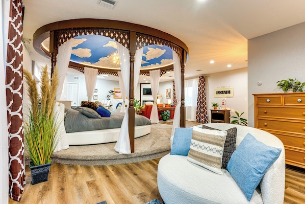 A bedroom with a curved canopy bed, a sofa, and a wooden dresser.