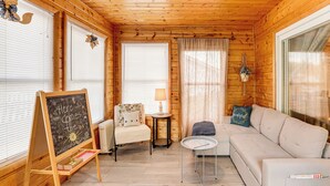 L’intérieur d’un chalet accueillant, avec un plafond en bois, un tableau noir sur lequel on a écrit, un canapé, un fauteuil et une petite table.