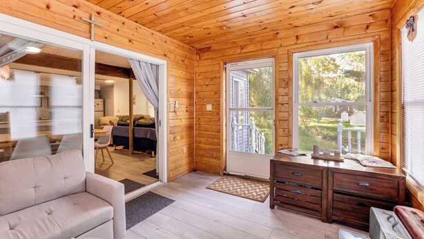 L’intérieur chaleureux d’un chalet, avec un plafond en bois, un canapé, une commode et une grande fenêtre donnant sur l’extérieur.