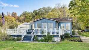 Une maison bleue avec un porche et des marches blancs, entourée d’arbres et d’une pelouse.