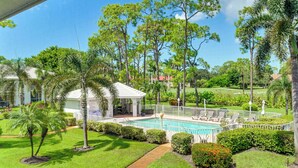 Zona de piscina con un pabellón, palmeras y un césped bien cuidado.