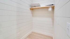 Ein Eckzimmer mit weiß getäfelten Wänden, Holzboden und einem Regal mit gefalteten Handtüchern und einer Decke.