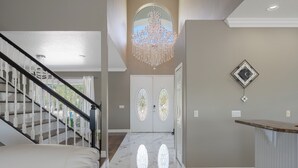 A hallway with a marble floor, a chandelier, a staircase, and a door with stained glass windows. - Pool and canal front home in Palm Coast! (Palm Coast)