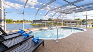 A covered outdoor swimming pool with lounge chairs and a view of buildings across the water. - Pool and canal front home in Palm Coast! (Palm Coast)