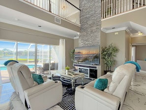 A spacious living area with a large TV, comfortable seating, a pool view, and a stone accent wall.