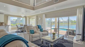 A spacious living room with a high ceiling, a dining area, and a view of a swimming pool. - Pool and canal front home in Palm Coast! (Palm Coast)