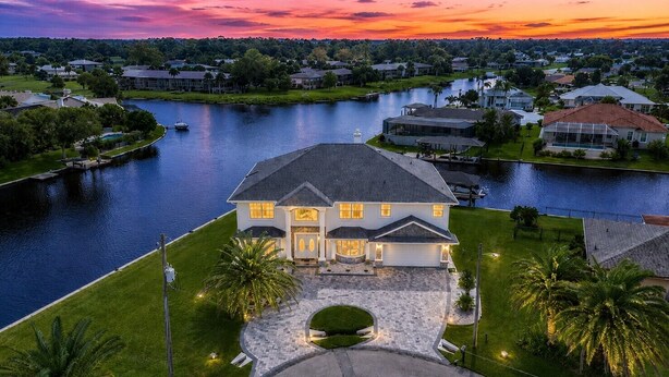 A large house with a driveway, a lawn, and a river in the background. - Pool and canal front home in Palm Coast! (Palm Coast)