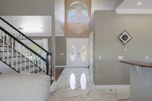 A hallway with a marble floor, a chandelier, a staircase, and a door with stained glass windows.