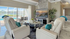 A spacious living area with a large TV, comfortable seating, a pool view, and a stone accent wall. - Pool and canal front home in Palm Coast! (Palm Coast)