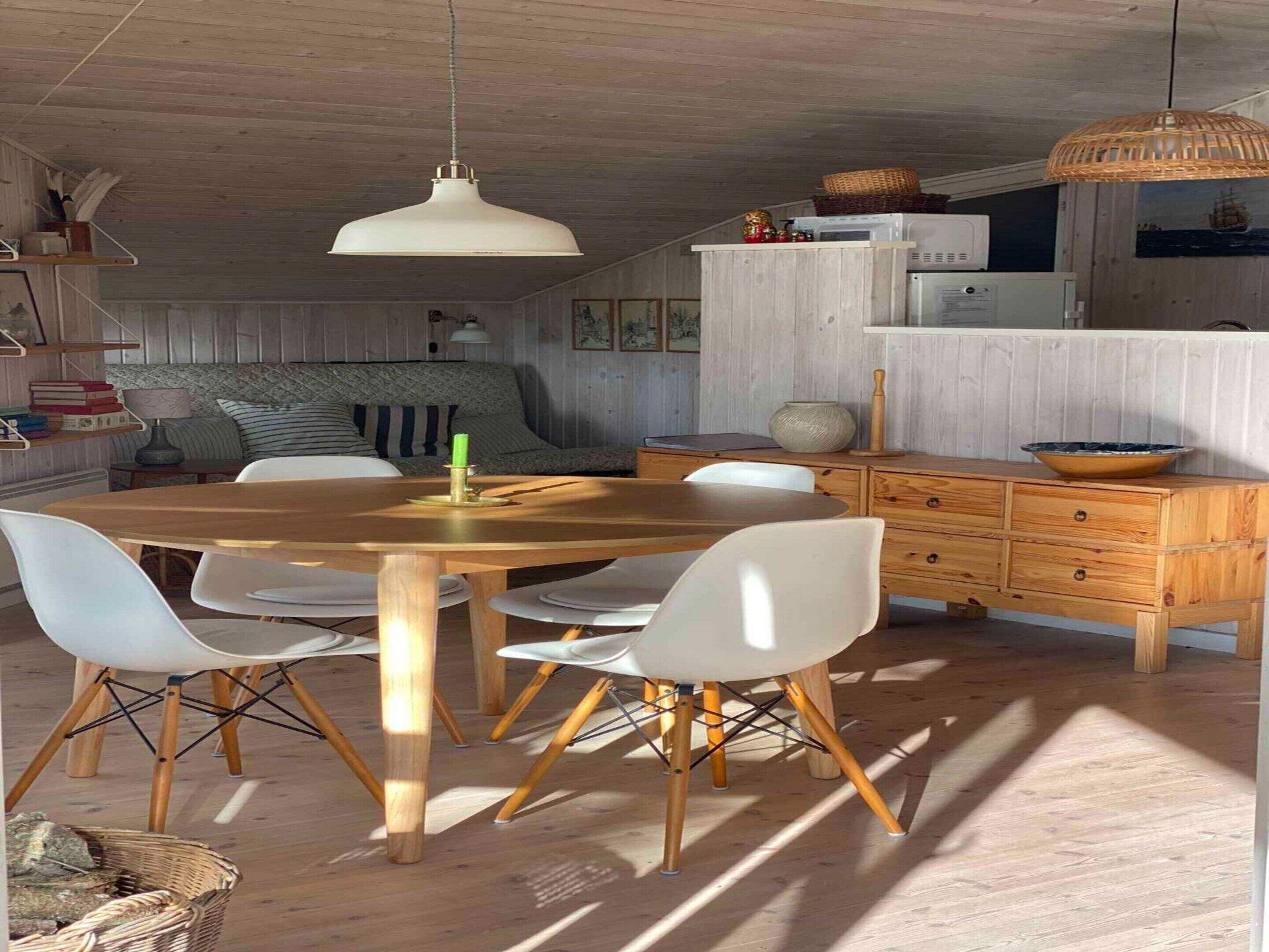 A dining area with a wooden table, white chairs, a hanging light fixture, and a wooden cabinet with a bowl on top.