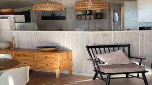 Une cuisine avec des meubles de rangement en bois, une table à manger et une chaise. Deux lampes en osier sont suspendues au plafond.