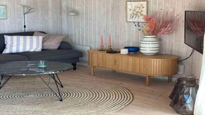 Un salon moderne avec un canapé foncé, une table basse ronde, une console en bois agrémentée d’objets décoratifs et un tapis à motifs.